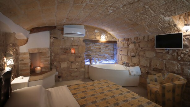 Quarto com paredes de pedra, lareira de pedra, banheira e televisão montada na parede.