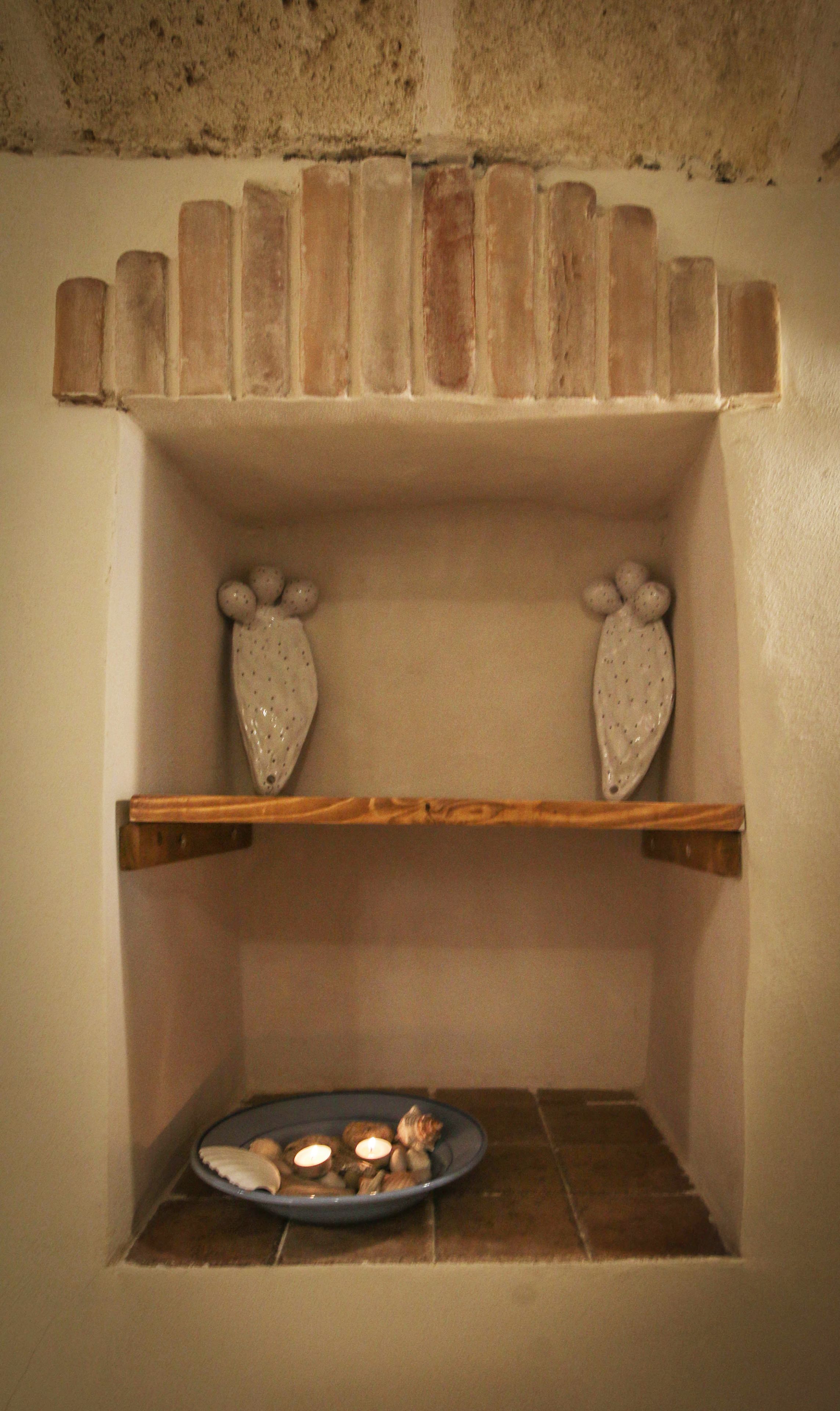 A stone fireplace with two decorative ceramic pieces on shelves and a tray with candles below.
