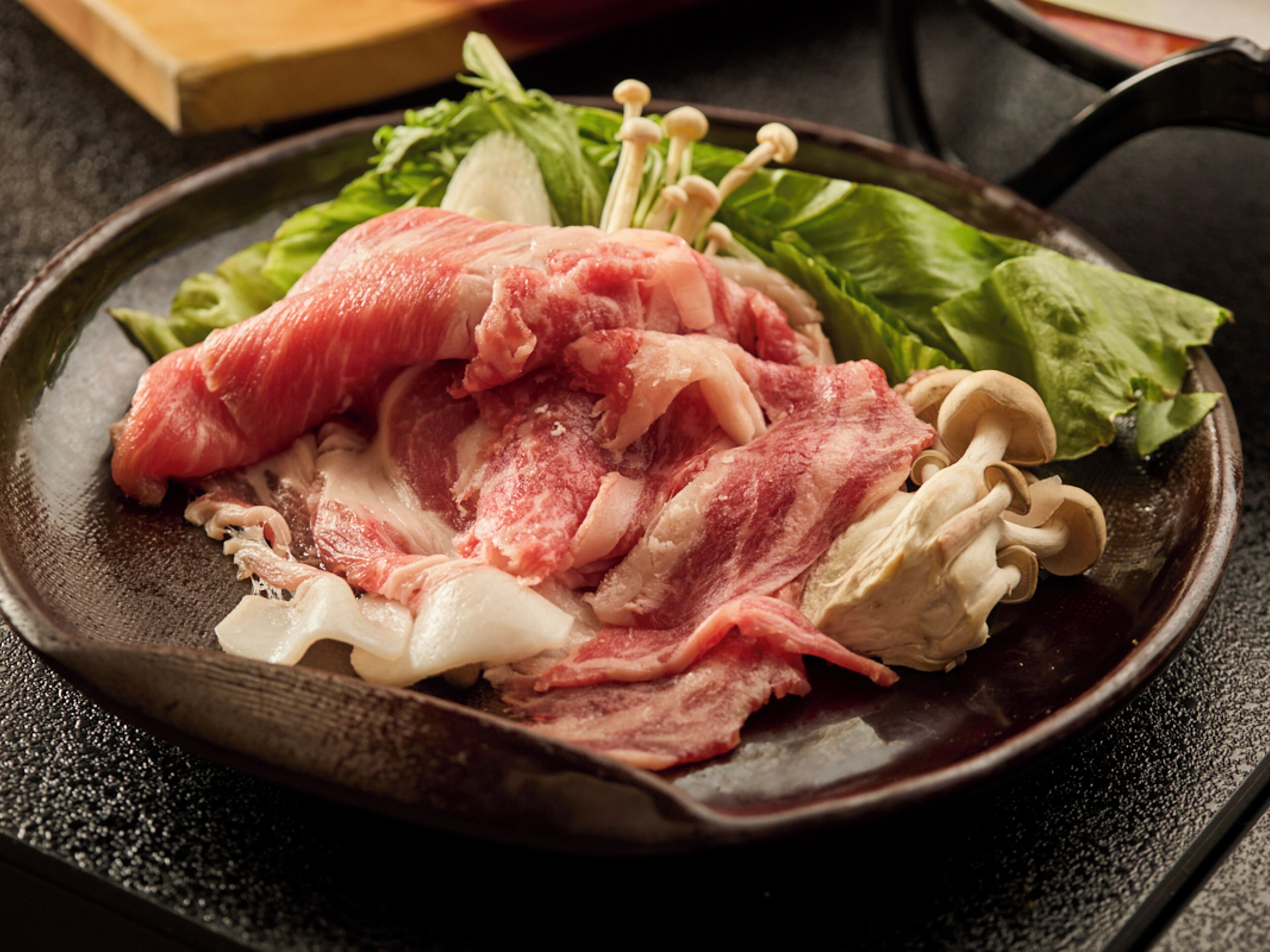 Une poêle contenant de la viande crue, des champignons et des légumes verts.