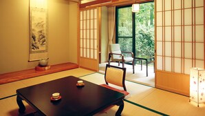 Una tradizionale stanza giapponese con pavimento in tatami, un tavolino con due tazze, una sedia e uno schermo scorrevole che dà su un giardino.