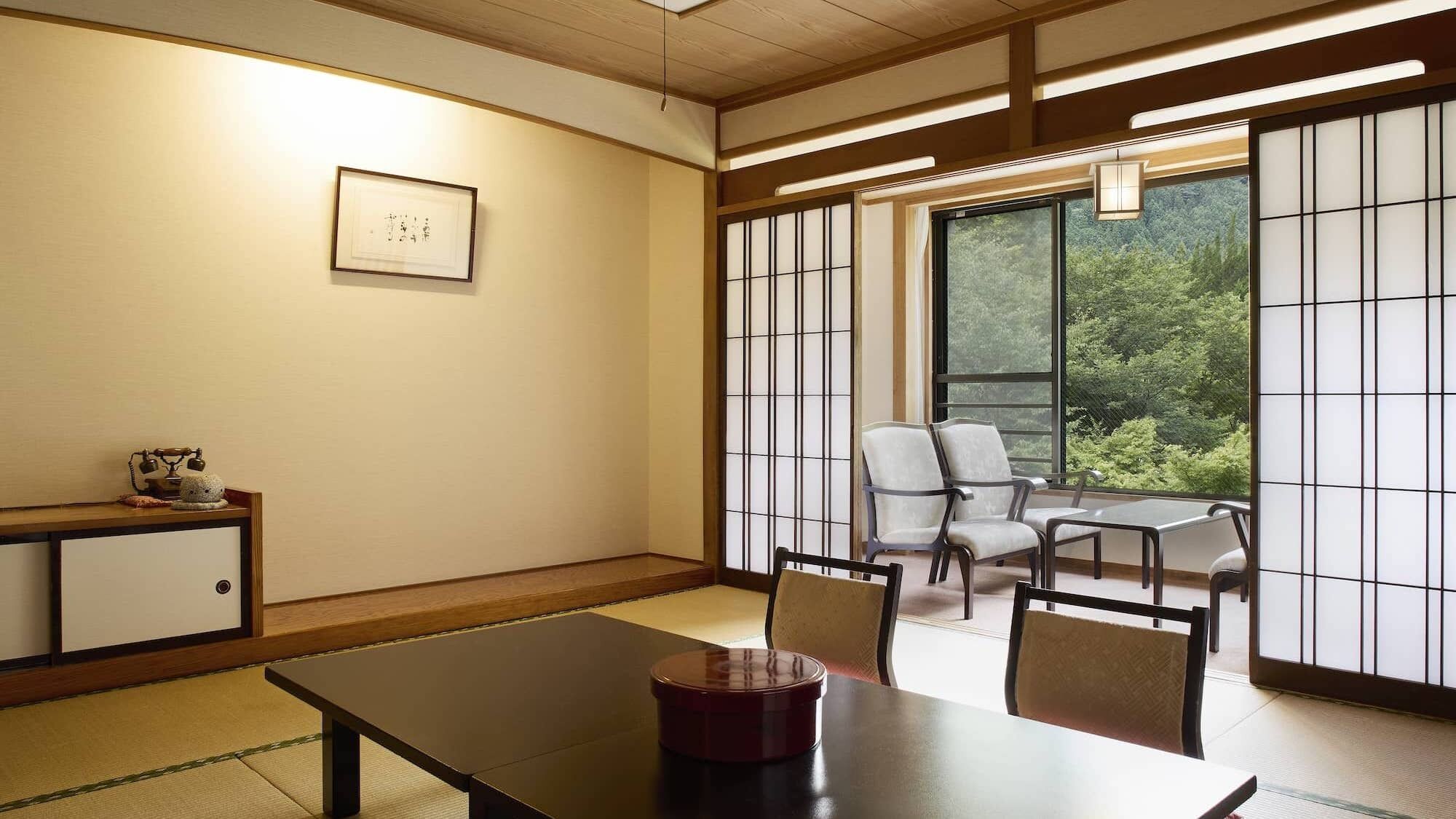 Een traditionele Japanse kamer met tatami vloeren, een lage tafel, stoelen, een shoji scherm en uitzicht op groen buiten.