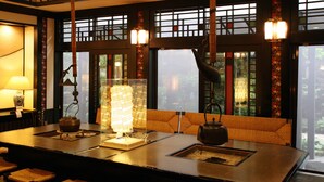Una tradizionale stanza in stile giapponese, con tatami, un tavolino e una teiera, e un'ampia finestra con vista sul verde.