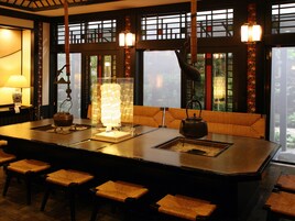 Um quarto em estilo japonês tradicional com esteiras de tatame, uma mesa baixa com um chaleira e uma janela grande com vista para vegetação.