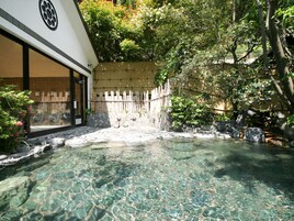 Piscina ao ar livre cristalina com borda de pedra, rodeada por cerca de madeira e vegetação exuberante.