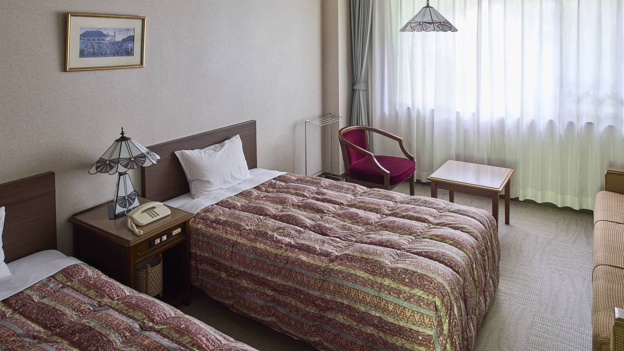 Een hotelkamer met twee bedden, een bureau, een stoel, een lamp en een hanglamp.
