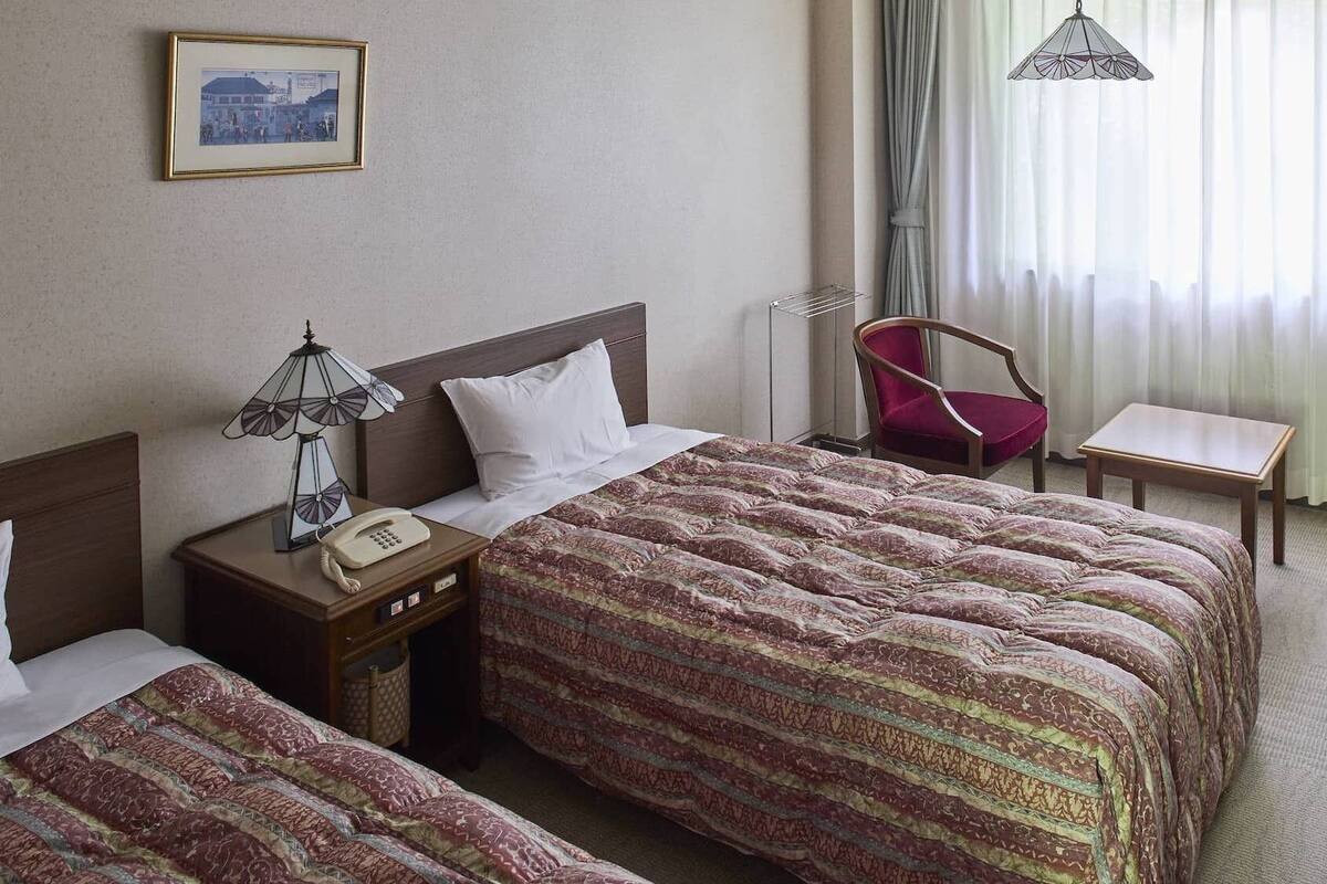 A hotel room with two beds, a desk, a chair, a lamp, and a hanging light fixture.
