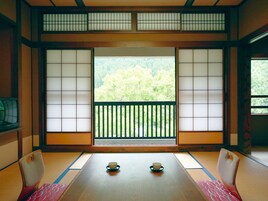 Um quarto japonês tradicional com tatames, biombos shoji e vista para uma área arborizada.