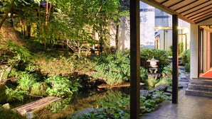 Un giardino tranquillo con un piccolo stagno, un ponticello di bambù e lanterne tradizionali giapponesi.
