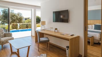 A modern hotel room with a wooden desk, a flat-screen TV, a sofa, and a view of a swimming pool.