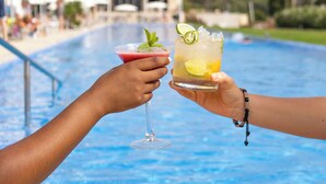 Two people toasting with drinks at a poolside.