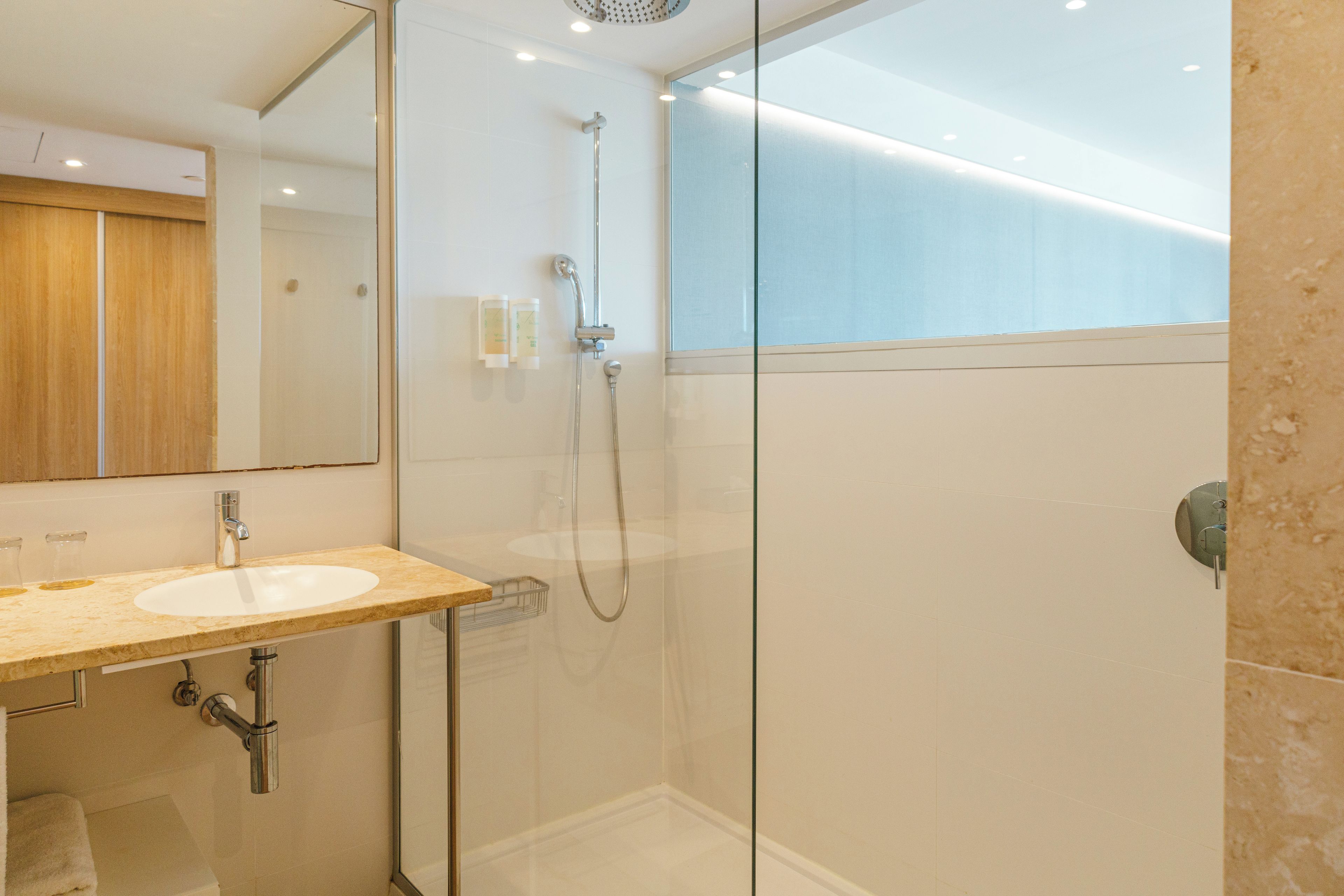 Un baño moderno con cabina de ducha de vidrio, lavamanos con encimera de mármol y espejo sobre el lavamanos.