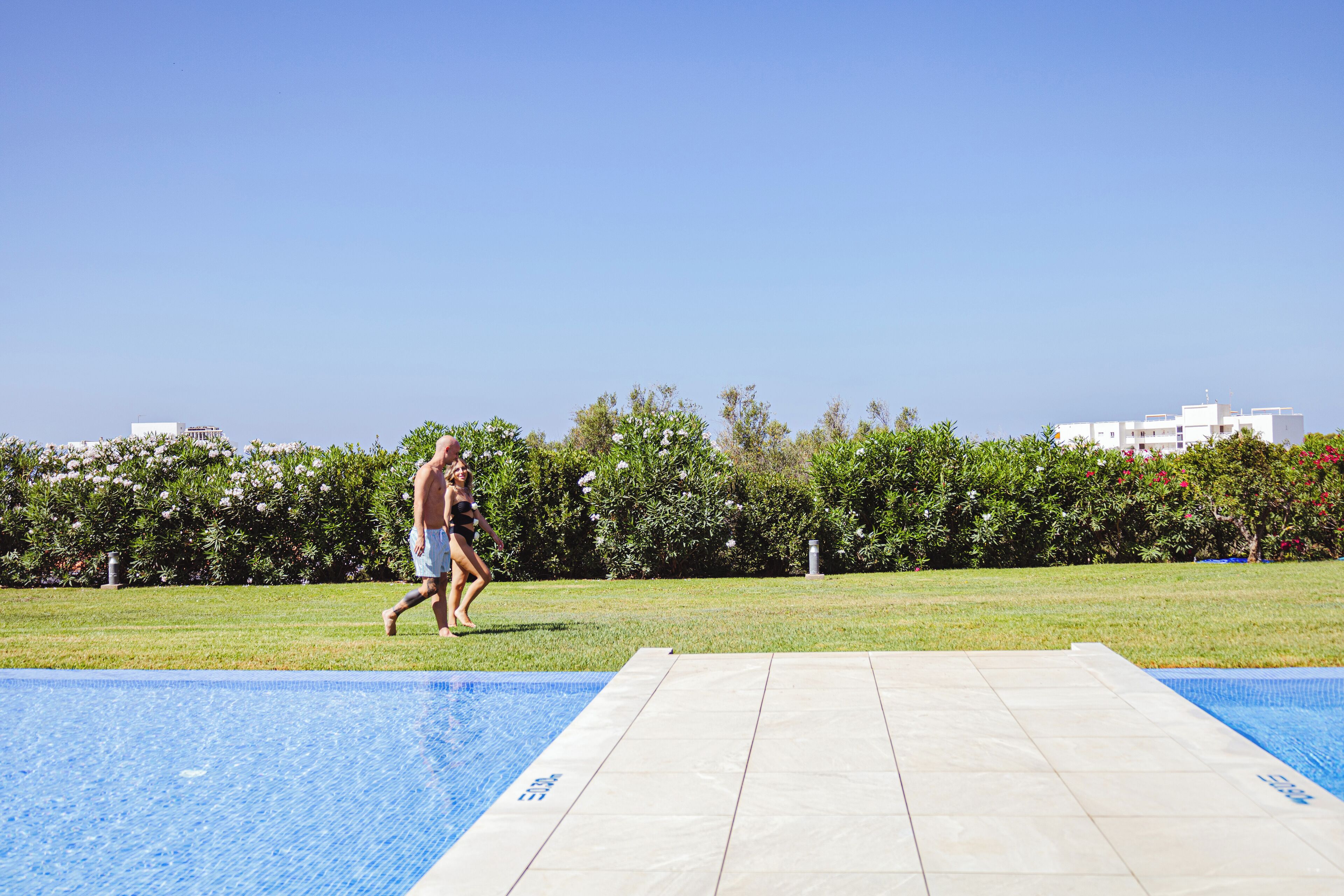 A swimming pool with a clear blue water surface, surrounded by a grassy area and a hedge.