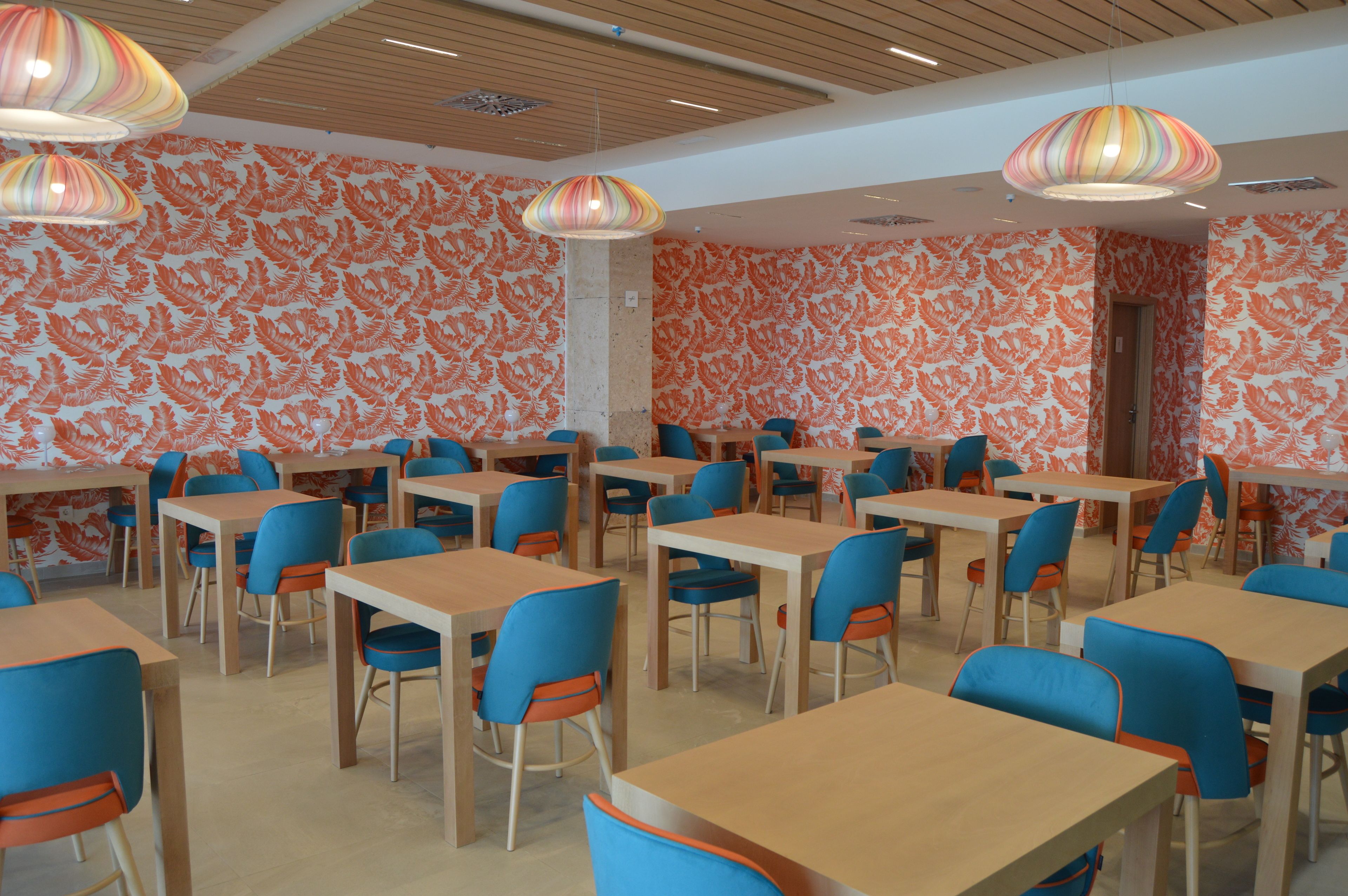 A dining area with tables and chairs, patterned wallpaper, and hanging lamps.
