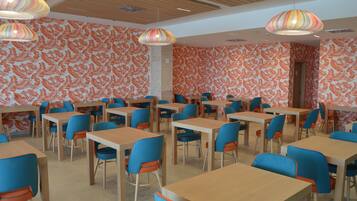 A dining area with tables and chairs, patterned wallpaper, and hanging lamps.