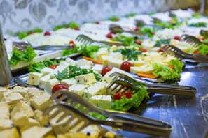 A buffet table with various cheeses, vegetables, and garnishes.