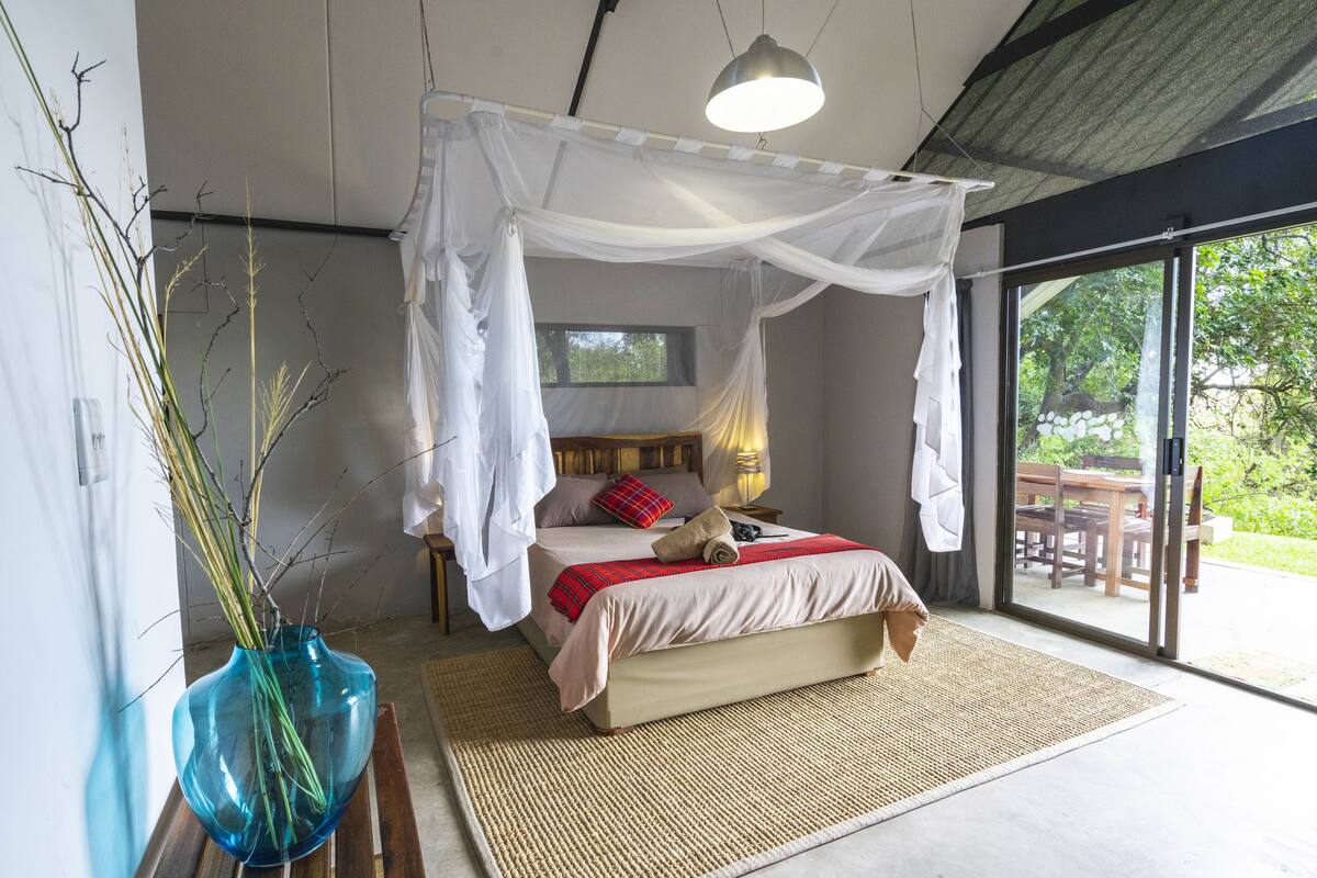 A bedroom with a canopy bed, a large window, and a view of the outdoors.