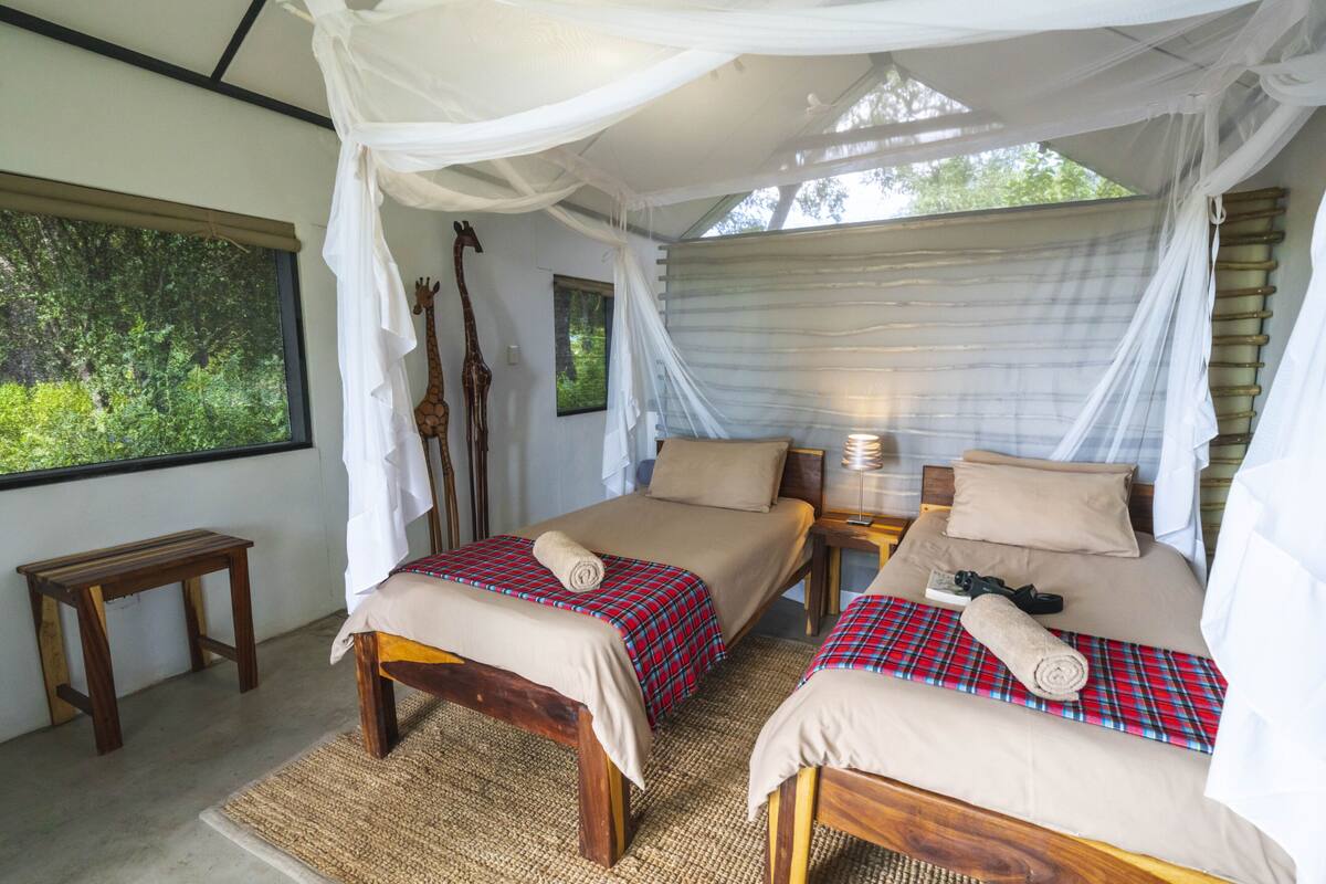 A room with two beds, a wooden bench, and a large window with a view of greenery.