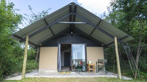 Un pequeño edificio de una sola planta, con techo inclinado, una puerta de acceso y un espacio al aire libre con mesa y sillas.