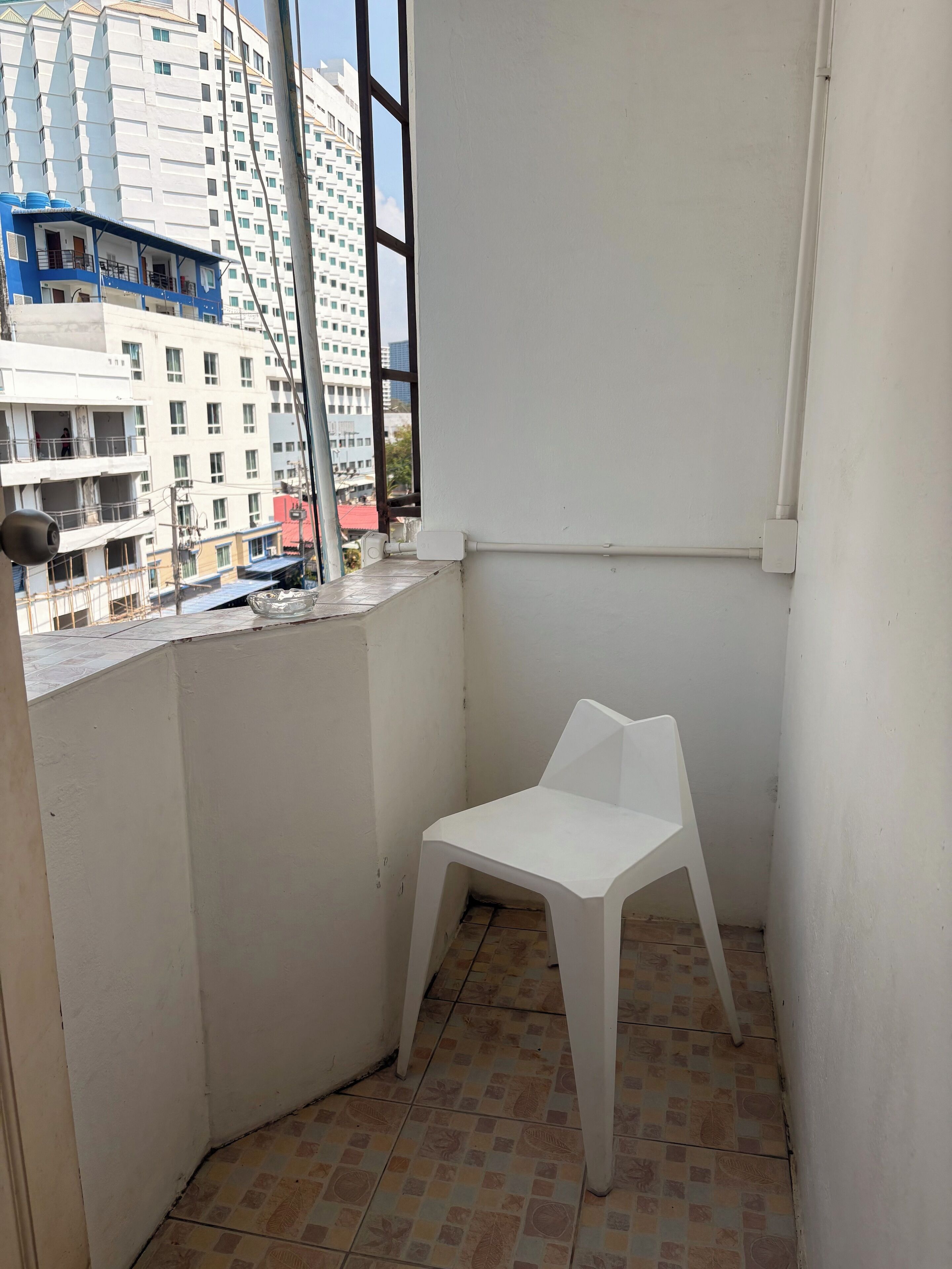 A small balcony with a white plastic chair, tiled floor, and a view of surrounding buildings.