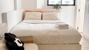 A minimalist bedroom with a bed, a bedside table, a window with a view, and a door. - Jellyfish Hostel (Pattaya)