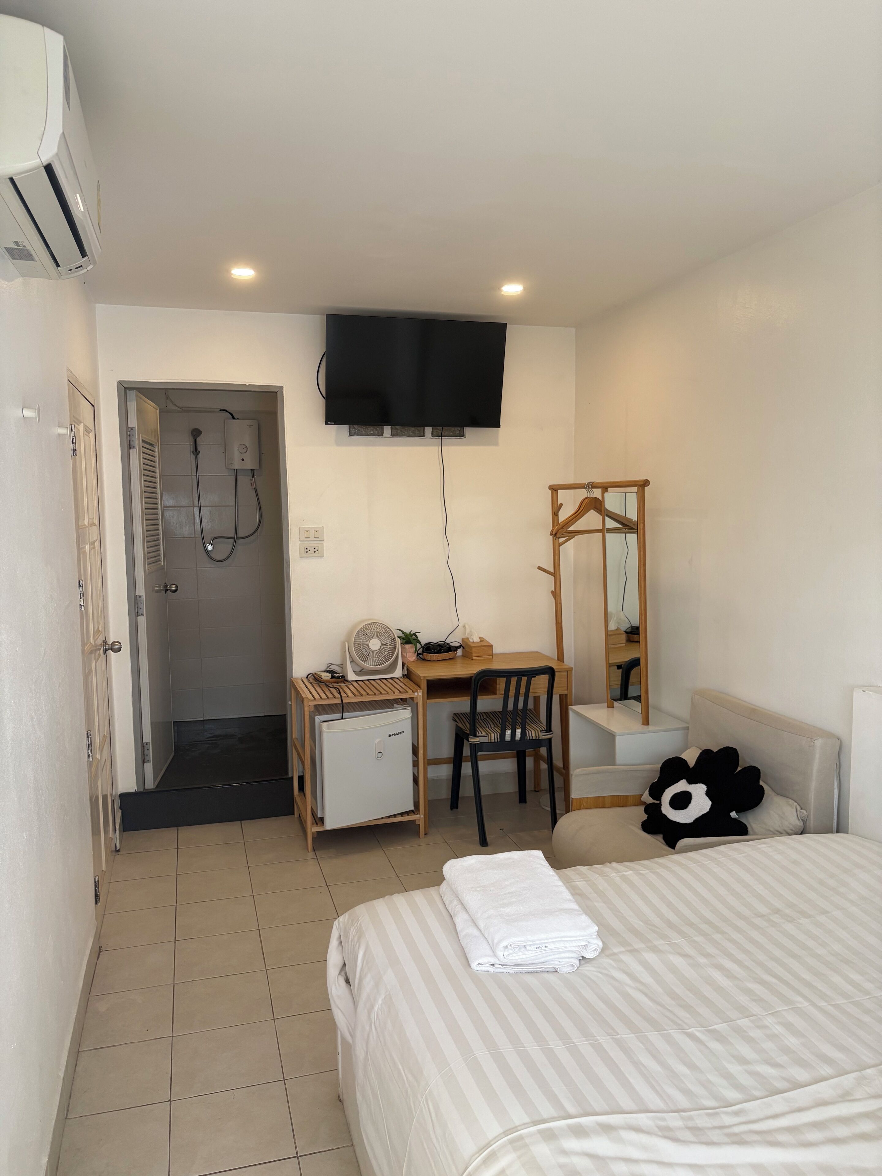 Habitación de hotel con cama, escritorio con silla, televisor, refrigerador pequeño, calefacción y zona de ducha.