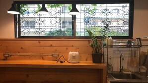A kitchen with a window, wooden counter, stools, a toaster, a potted plant, and a sink. - Jellyfish Hostel (Pattaya)