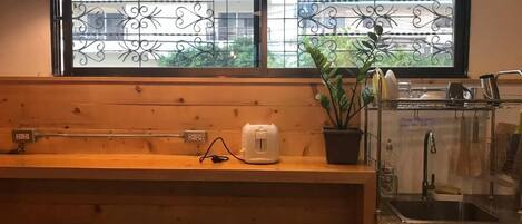 A kitchen with a window, wooden counter, stools, a toaster, a potted plant, and a sink.