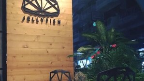 A wooden wall with a geometric logo and the text "JELLYFISH" in a restaurant setting with two black chairs and a small table. - Jellyfish Hostel (Pattaya)