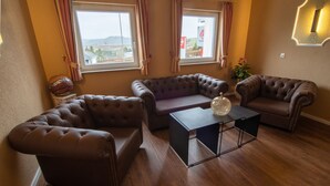 Una sala de estar con un sofá de cuero marrón, una pequeña mesa de centro y dos ventanas con cortinas.