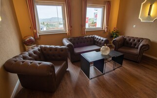 Una sala de estar con un sofá de cuero marrón, una pequeña mesa de centro y dos ventanas con cortinas.