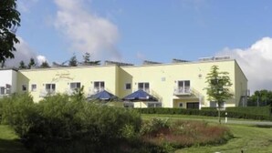 Un hotel de dos plantas con fachada amarilla, múltiples ventanas y sombrillas exteriores.