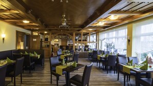 Un restaurante con vigas de madera, mesas con manteles individuales verdes y una zona de bar.