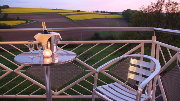 Un balcón con una mesa lista para dos personas, una silla y vistas a campos y árboles.