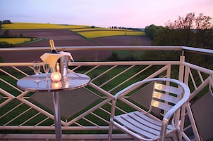 Un balcón con una mesa lista para dos personas, una silla y vistas a campos y árboles.