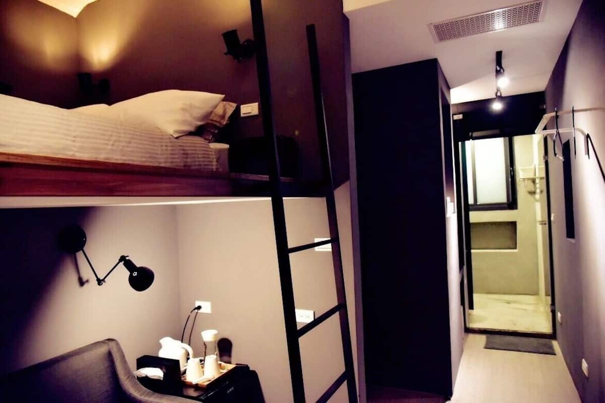 A compact room with a bunk bed, a desk with a lamp, and a shower area.