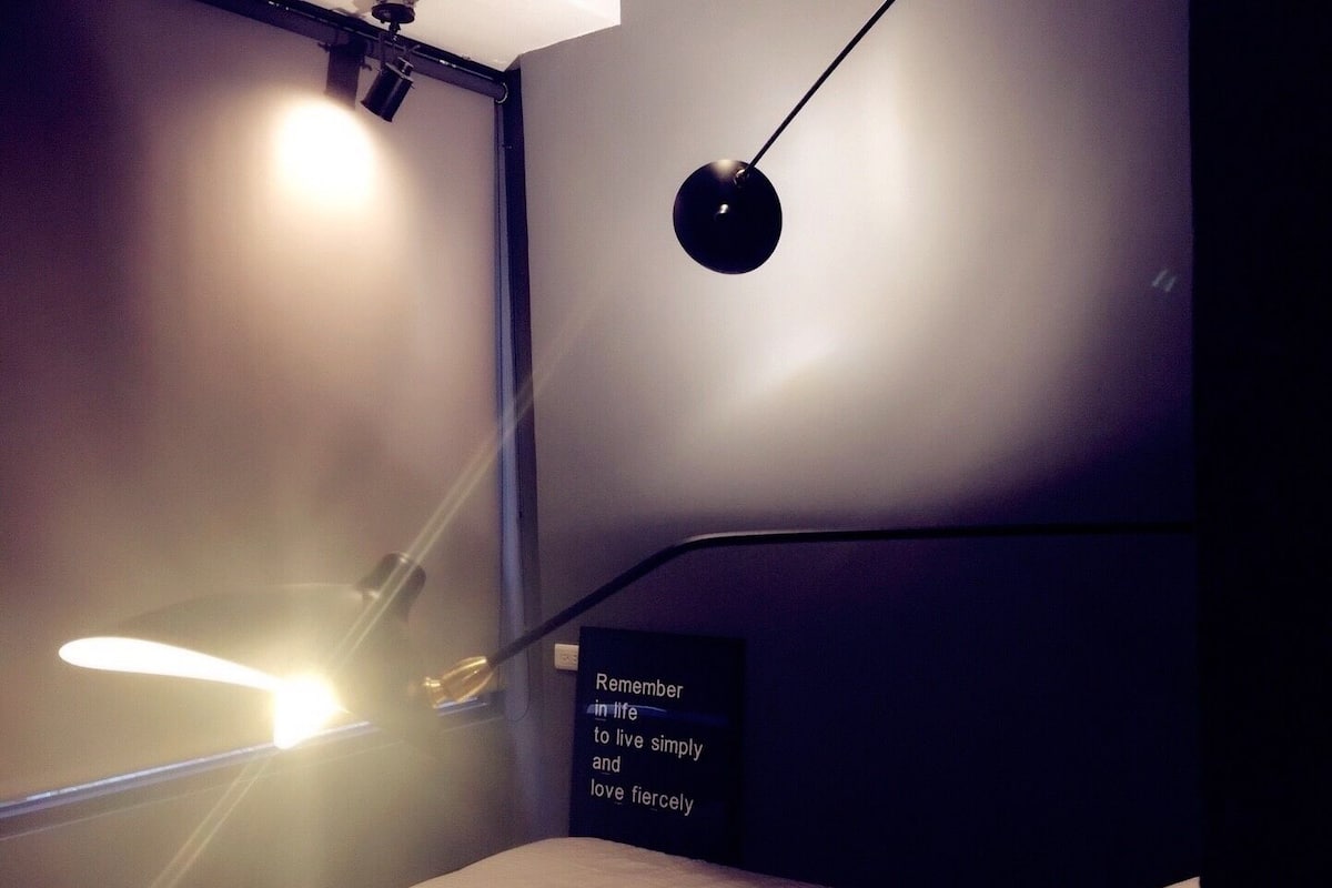 A dimly lit room with a bed, a wall-mounted light, and a sign with a quote.