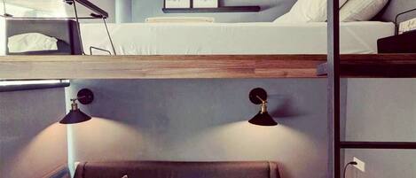 A compact room with bunk beds, a sofa, a bedside table, and a lamp.