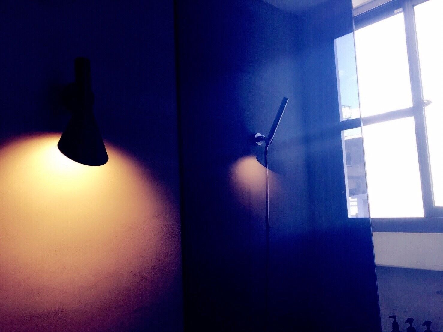 Um quarto com janela, porta e luminária fixada na parede.