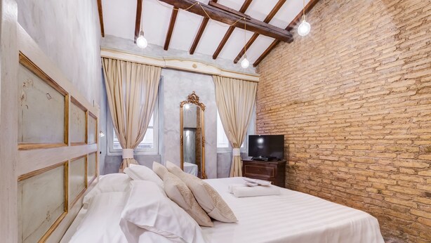 A bedroom with a large bed, wooden beams, a brick wall, a TV, and curtains. - Colonna Suite - Spanish Steps Suite & Spa (Rome)