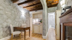 A dining area with a wooden table and chairs, a kitchen with white cabinets, and a wooden ceiling. - Colonna Suite - Spanish Steps Suite & Spa (Rome)