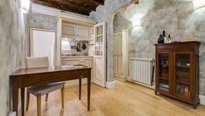 A kitchen with white cabinets, a wooden table, and a cabinet with glass doors. - Colonna Suite - Spanish Steps Suite & Spa (Rome)