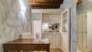 A compact kitchen with white cabinets, a wooden table, and a marble wall. - Colonna Suite - Spanish Steps Suite & Spa (Rome)