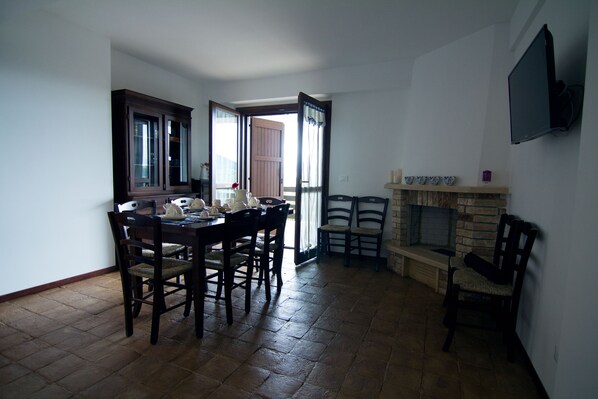 Un comedor con una mesa y sillas de madera, una chimenea y un televisor fijado a la pared.