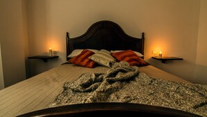 Ein ordentlich bezogenes Bett mit einem dunklen Kopfteil, zwei Nachttische mit Kerzen und eine Decke auf dem Bett.