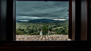 Blick durch ein Fenster mit Ziegeldach auf ein Tal mit Feldern und fernen Bergen.