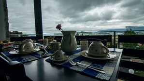 Ein Tisch ist gedeckt mit Teetassen, einer Kanne und Besteck auf einer blau gemusterten Tischdecke, mit Blick auf eine reizvolle Landschaft.
