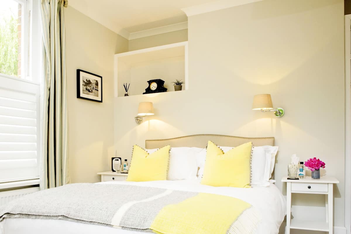 A neatly arranged hotel room with a large bed, two bedside tables, a nightstand, a wall-mounted clock, a framed picture, and a window with curtains.