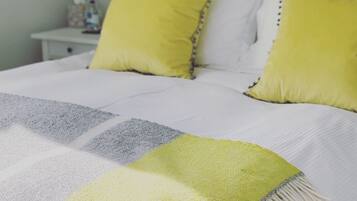 Ein ordentlich bezogenes Bett mit einer weiß-grauen Streifendecke und einer gelben Tagesdecke.
