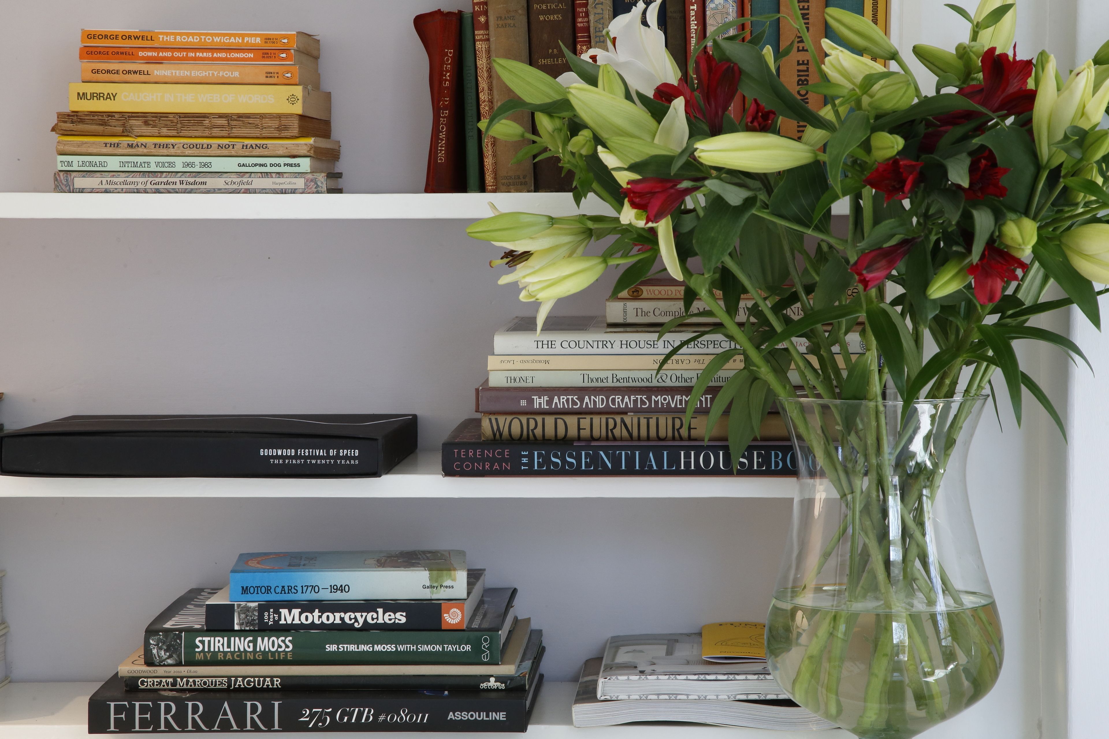 A bookshelf with various books and a vase with flowers.