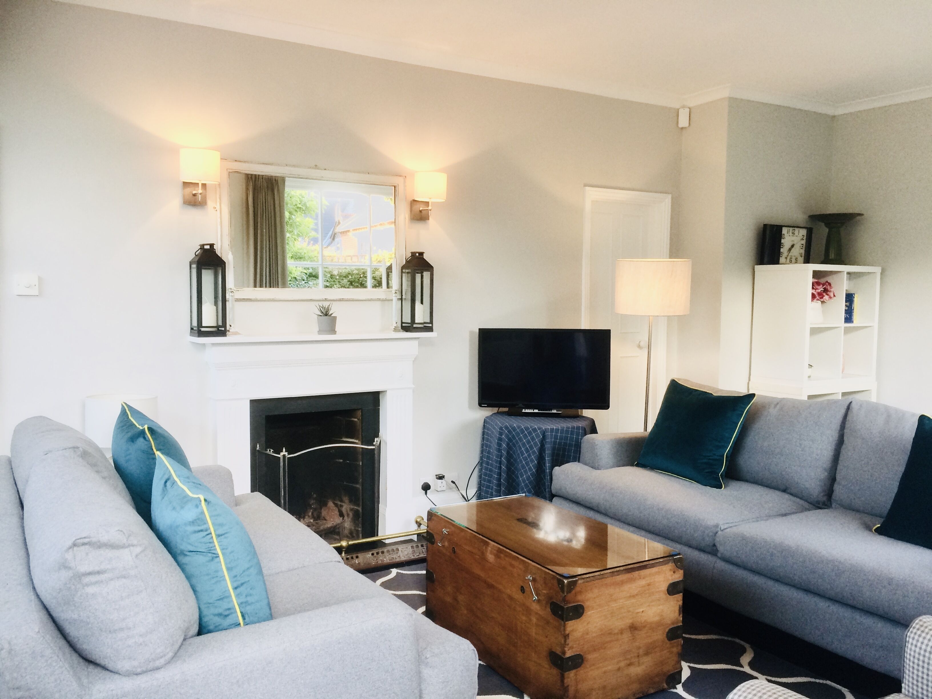 A living room with a fireplace, two grey sofas, a wooden chest, and a television.